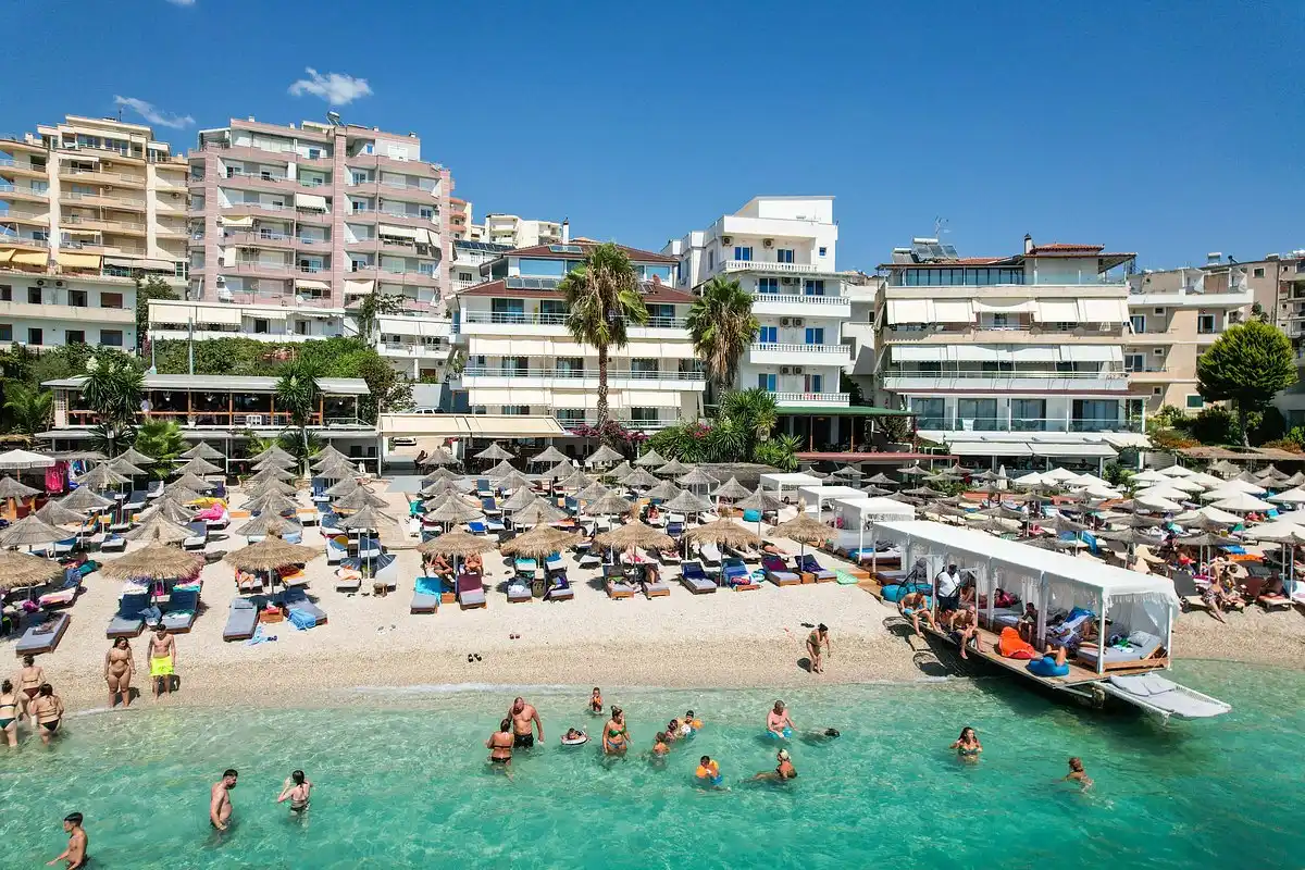 Straw umbrellas and sunbeds on a busy beach in Saranda, with turquoise water and seafront hotels